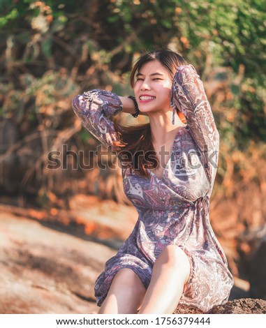 Young Asian woman is relaxing on a rock on a Sunny Beach for Summer vacation relaxation and hapiness concept.