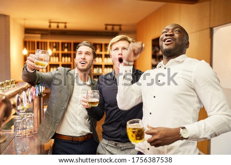 Friends as fans watch a football game together in the pub and cheer enthusiastically Royalty-Free Stock Photo #1756387538