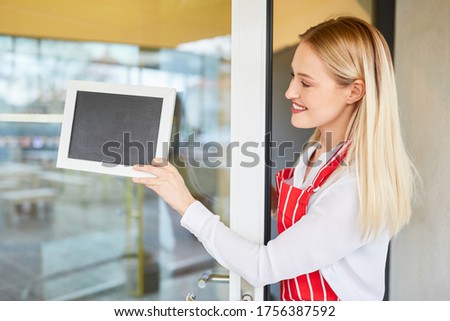 Waitress hangs a blank chalkboard on the door of a restaurant
