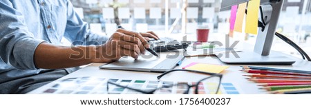 Image of male creative graphic designer working on color selection and drawing on graphics tablet at workplace with work tools and accessories in workspace.