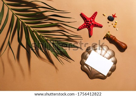 Empty business card, red sea star, tropical green palm leaf decor and sealing wax stamp. Summer trendy flat lay on warm ochre orange background. Minimal mockup template. Creative nature composition