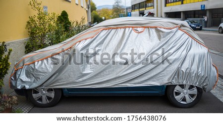 car is protected from weather by tarpaulin.