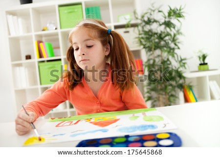 red-haired girl with pigtails drawing with watercolors on the paper his house