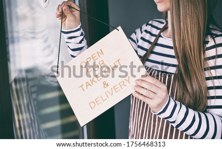 Woman holds the wooden sign with text: Open for take-out and delivery