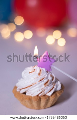 festive cupcake with a purple star-shaped candle. On the background of red gift box with a pink ribbon, multi-colored balloons and lights. party, birthday concept. Copy space. . High quality photo