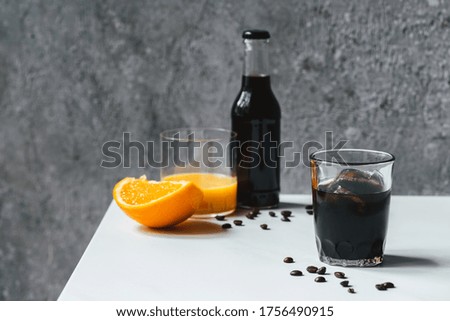 selective focus of cold brew coffee with ice in glass and bottle near orange juice and coffee beans on white table