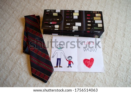 Happy fathers day greeting card with writing I love U you Daddy, red heart and drawing father and child holding hands wearing face mask, gift bag for bottle, red striped dark tie as presents on bed