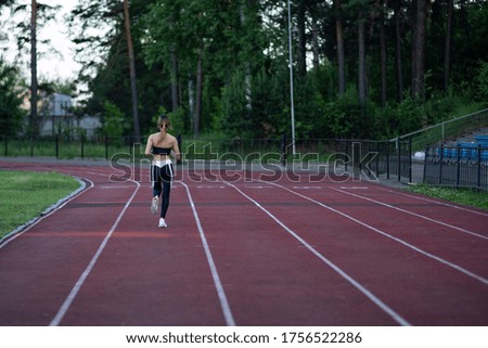 The girl is jogging around the stadium. Caring for health and fitness. Photo of a brunette from the back engaged in jogging