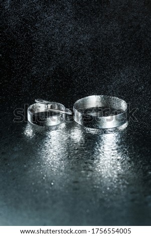 Beautiful wedding silver rings on dark wet glass with water drops.