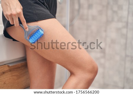 Cropped photo of a young female in shorts massaging her leg with a plastic roller massager