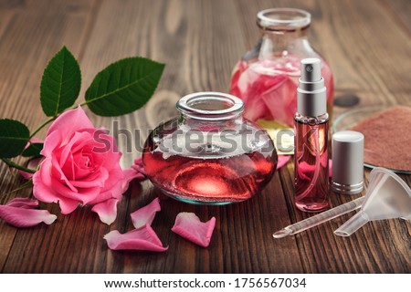 Rose flower, infused water and essential oil or rose blend bottle, flavored water in a spray bottle, pink clay powder, glass spatula and small funnel for making of cosmetic products at home. Royalty-Free Stock Photo #1756567034
