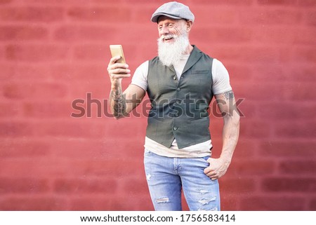 Image of caucasian man holding mobile phone isolated over wall red background. Hipster man holding smartphone far from his ear. Happy man to listen and looking the video on the cell phone.  Image