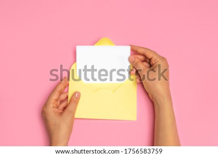 Top view of woman hands holding empty white card and open yellow envelope letter on pink background, mockup Royalty-Free Stock Photo #1756583759
