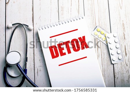 On a light wooden table are a stethoscope and blisters with pills, and between them is a notebook on which detox is written in red