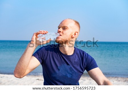 Young male athlete dring fresh water from plastic bottle on the beach
