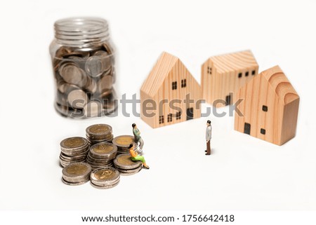 Miniature figure standing and sitting on stacked coin with bottle coin and wooden house isolated on white background, concept planning savings money for buy a house.