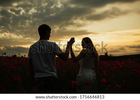 Young couple holding hands and looking at each other on sunset in the warm summer day. The couple holding hands at sunset in the field. Copy space.