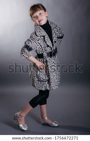 Little girl in leopard print coat, black leggings and silver shoes against a dark background in smoke