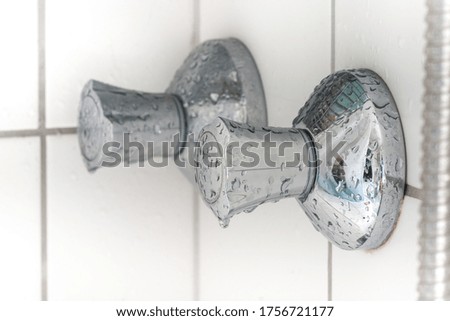 Bathroom faucet with chrome plating, water drops, white tiled background.