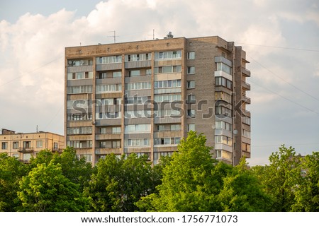 Typical facade of an old brick nine-story building in the post-Soviet countries on a background of green trees. Royalty-Free Stock Photo #1756771073