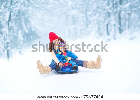 Young happy mother and her little toddler daughter enjoying a sledge ride in a beautiful snowy winter park