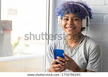 young woman afro american with headphones and mobile phone at the window