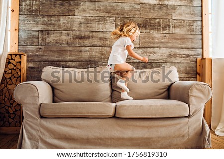 Lifestyle image of a little girl having fun and jumping on a sofa at home.