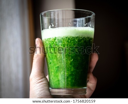 Picture of hand holding glass of green smoothie. Sirtfood diet concept.
