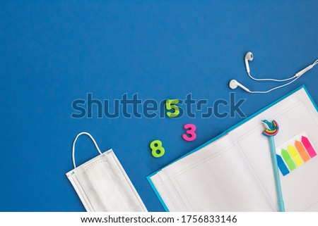 Flat lay back to school coronavirus. Open notepad, pen, bookmark stickers, bright numbers, headphones, protective mask on a blue background.