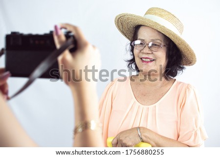 60s old woman is smiling and wearing hat for traveling. She standing on white background and taking photos.