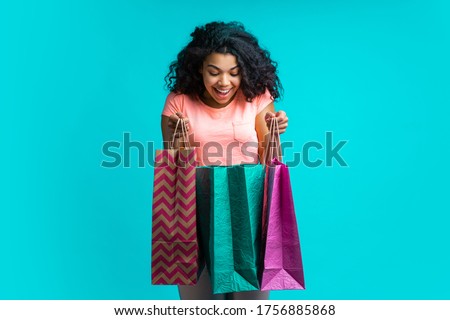 Smiling excited dark skinned girl looking into one of the shoping bags she's holding checking her purchase. Royalty-Free Stock Photo #1756885868
