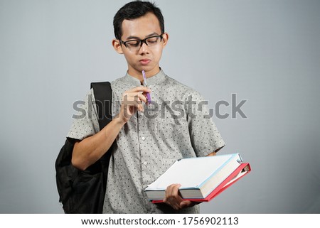 Young Asian male student wearing grey clothes with grey background.