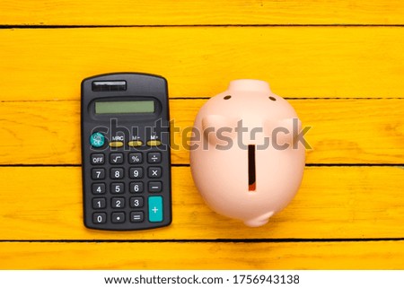 Piggy bank and calculator on a yellow wooden background. Top view