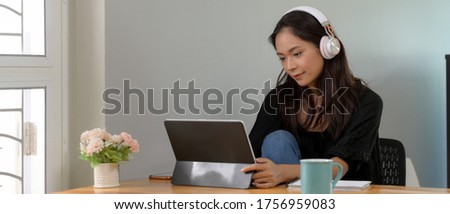 Cropped shot of female professor online teaching with digital tablet and headphone on wooden worktable in living room 