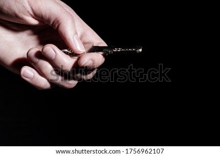 Close-up female hand holds a house key isolated on black background, low key