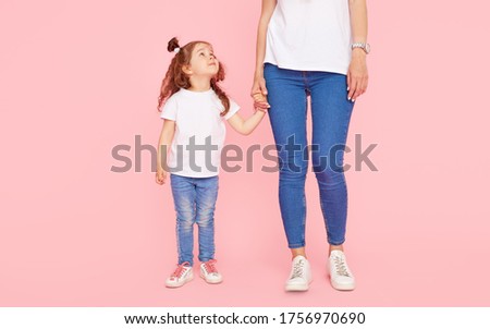 Family values. Mom and daughter in white t-shirts and jeans play and hug on a pink background. Caring for loved ones. Happy motherhood