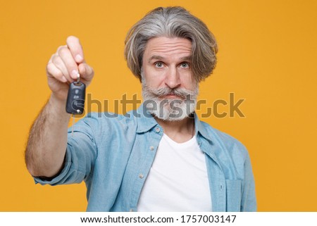 Elderly gray-haired mustache bearded man in casual blue shirt posing isolated on yellow wall background studio portrait. People sincere emotions lifestyle concept. Mock up copy space. Hold car keys