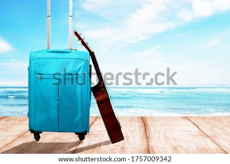 Blue suitcase with a guitar on a wooden floor with ocean view background