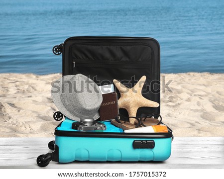 Suitcase with different beach objects on grey wooden table near sea