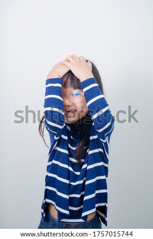 Close up head shot portrait image of stressed scared little girl. Concept unhappy, terrified and nervous kid feeling fear and cover mouth with hands on gray background, six year child looking at