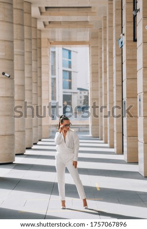 Elegant girl in a business suit with glasses stands against the background of the business center. The concept of expensive life vertical photo.