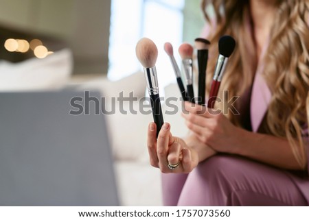 Attractive female make-up artist streaming on a laptop. Beauty blogger talking about various / different makeup brushes and shows them to her subscribers online
