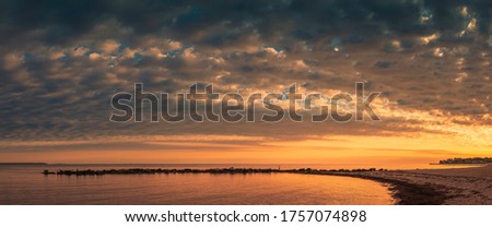 Panoramic cloudscape over the beach at dawn. Curved cove with cormorants on the rocks on Cape Cod Beach.