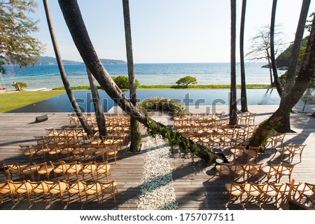 the amazing wedding venue prepared many rattan chairs for the wedding guests to sitting under the sunshine,the wedding ceremony area on the wooden floor near by the pool next to the ocean Royalty-Free Stock Photo #1757077511