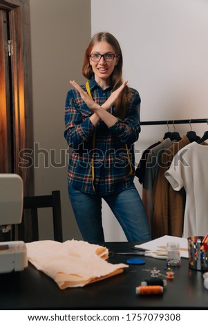 Smiling fashion designer looking at camera at workplace, dressmaker, seamstress or atelier owner sitting at table with sketches of fashion design, small business concept