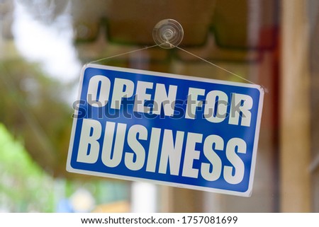 Close-up on a blue open sign in the window of a shop displaying the message "Open for business".
