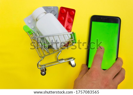 Online pharmacy. Closeup of hands on a phone and a mini shopping trolley with tablets. A woman chooses medicines on the Internet with home delivery
