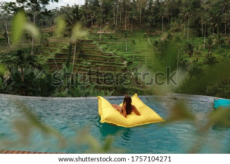 Beautiful young girl relaxing in swimming pool, woman swims on inflatable mattress and has fun in water on family vacation, tropical holiday resort, back view. Summer vacation