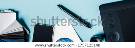 Panoramic shot of graphics tablet, smartphone and color samples on blue background