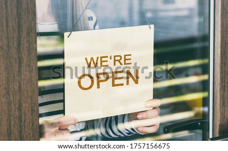 Woman holds the wooden sign with text: we're Open 